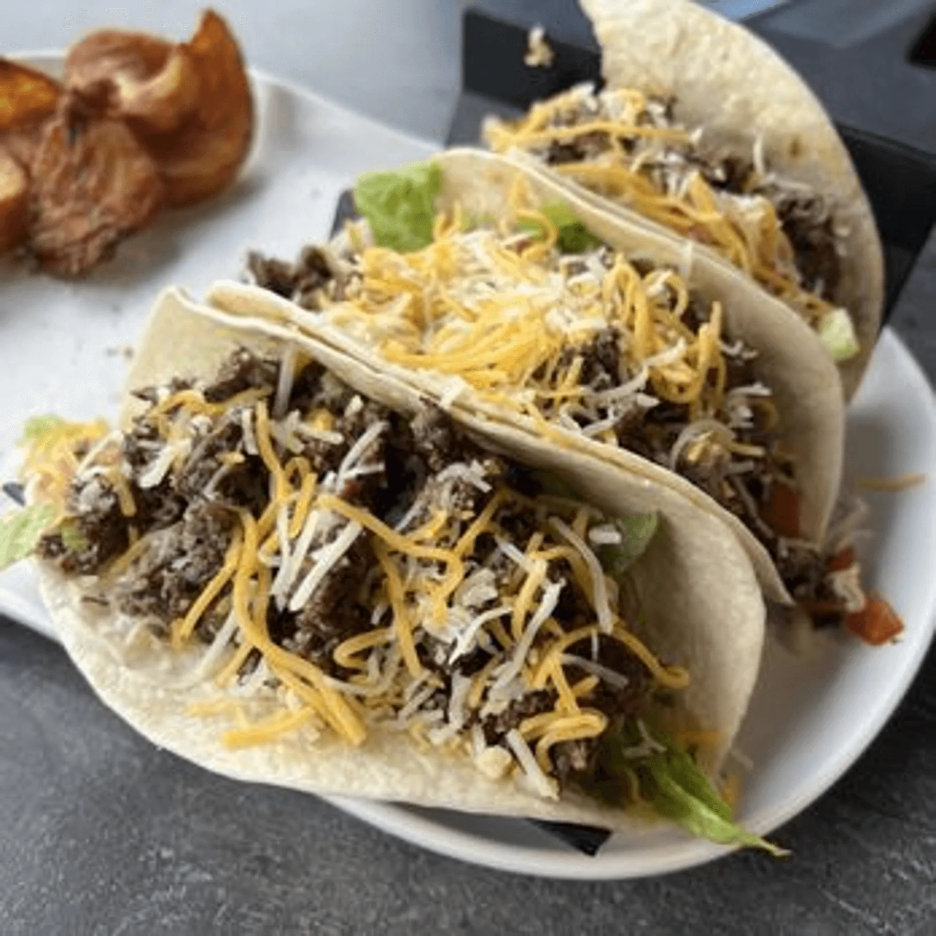 Three ShortyonDeck beef tacos with shredded cheese and lettuce, served with potato chips.