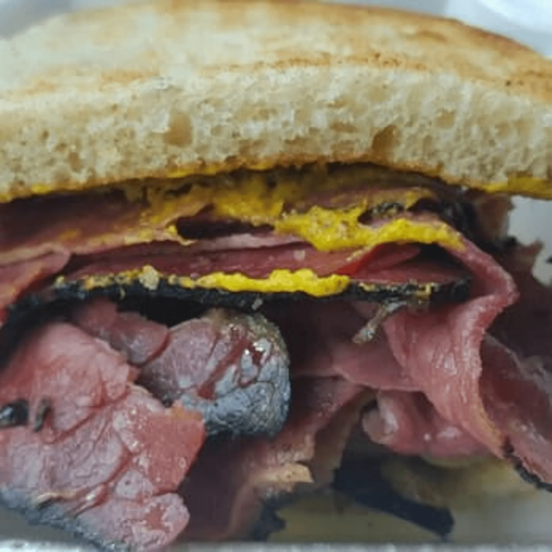 Close-up of a ShortyonDeck pastrami sandwich with mustard on toasted bread.