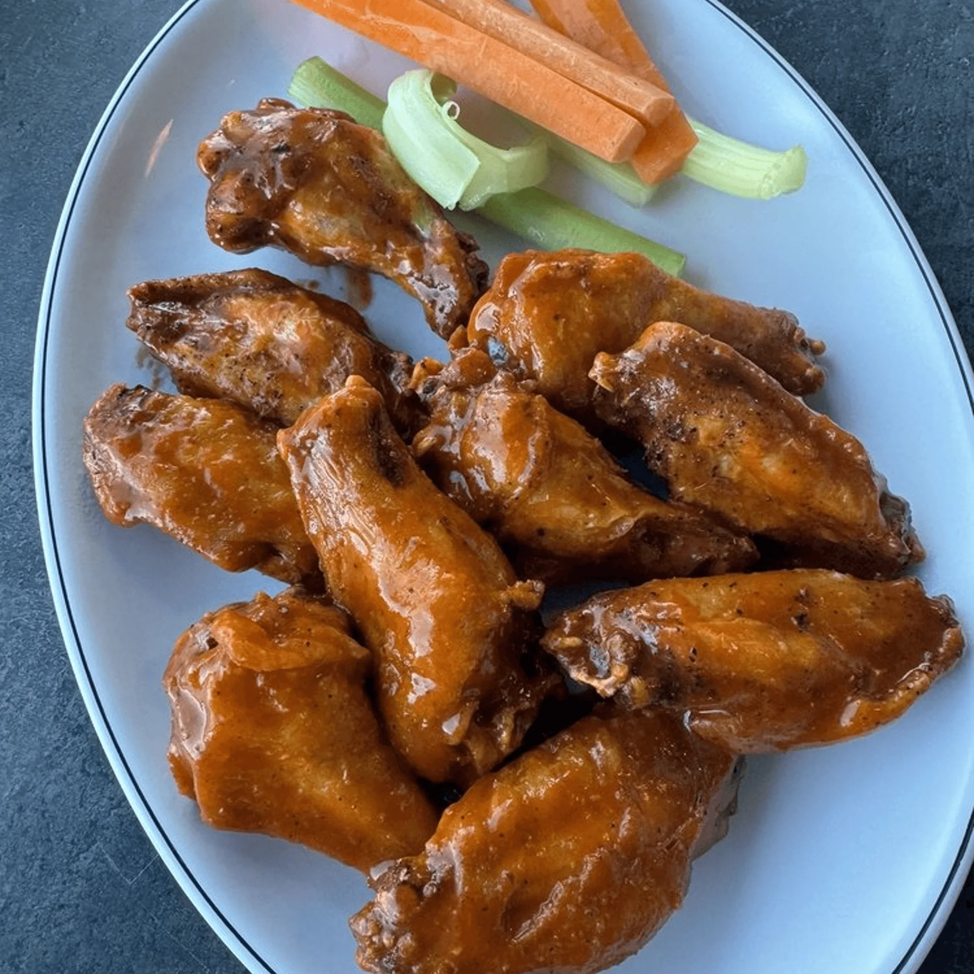 ShortyonDeck's American-style chicken wings, glazed in sauce, with carrot and celery sticks on a white plate.
