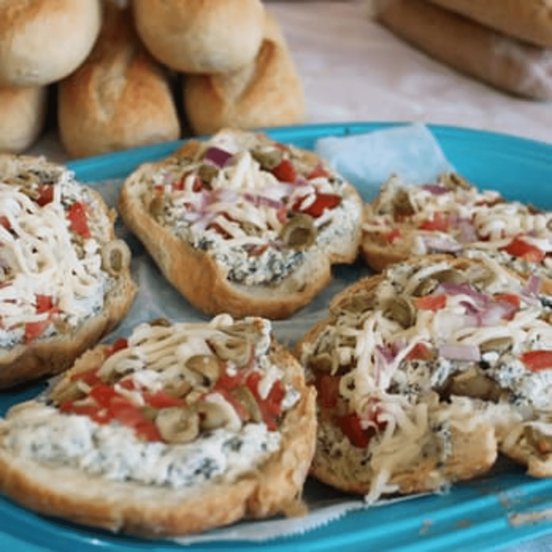 Open-faced sandwiches with cream cheese, olives, red peppers, and onions on a blue tray.