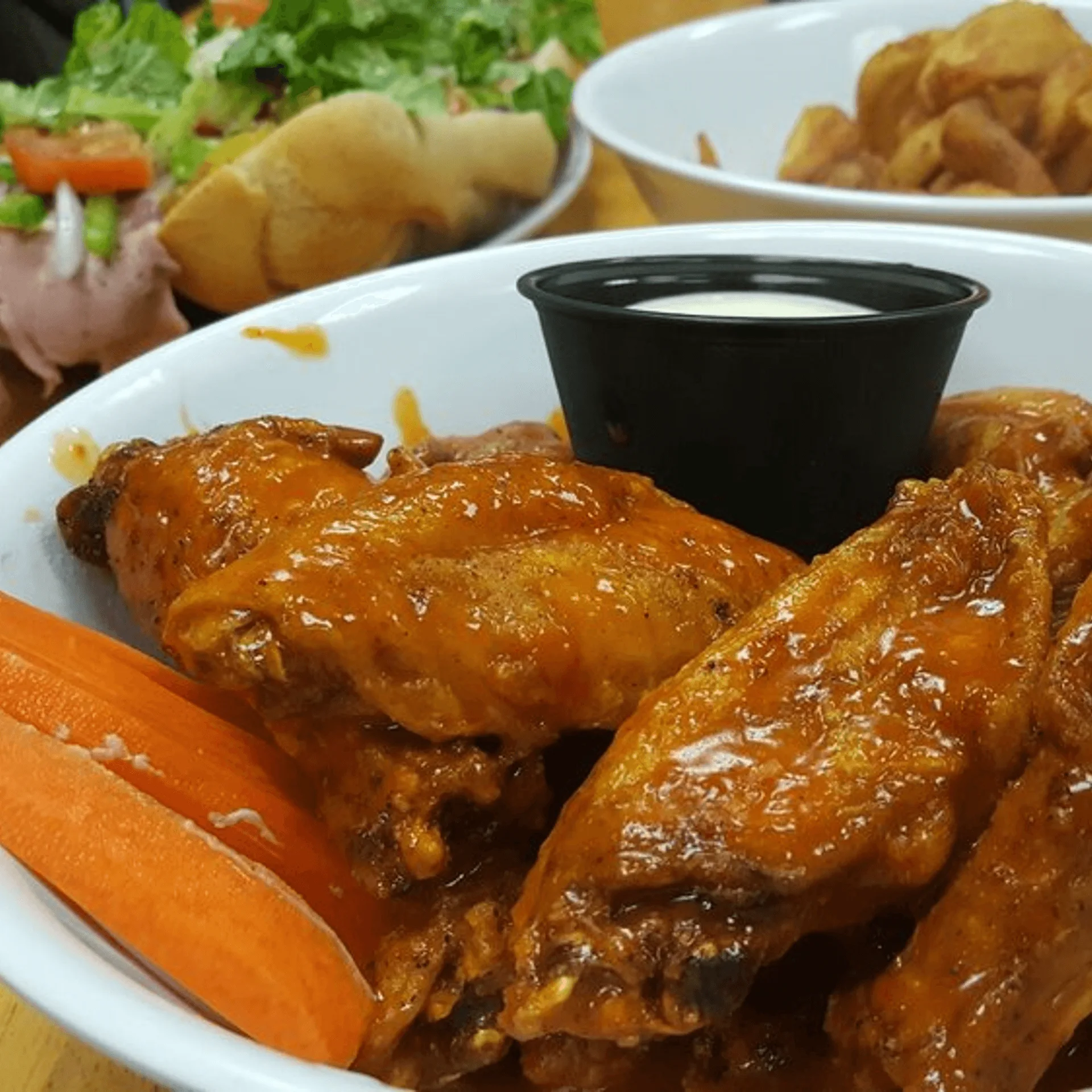 ShortyonDeck's buffalo wings with carrot sticks and ranch dressing, with a salad and fries in the background.