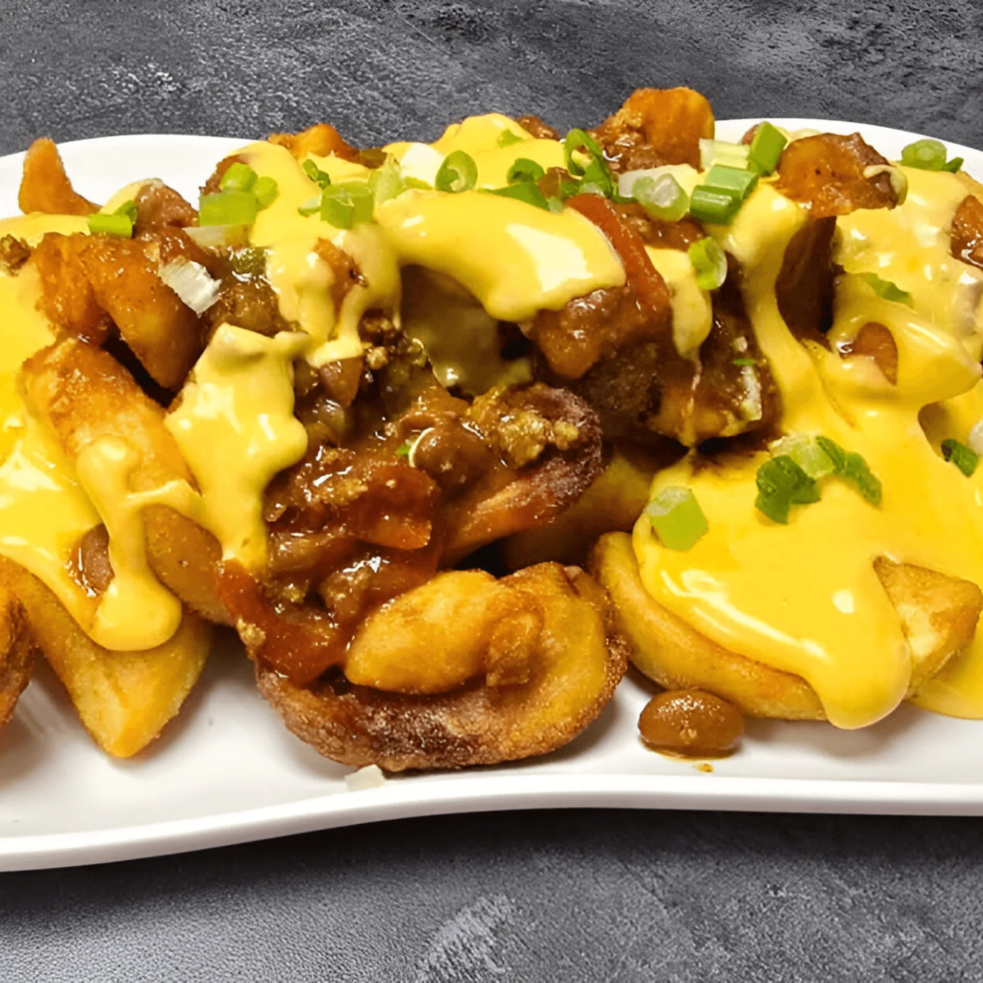 Chili cheese fries with chopped green onions on a white plate at ShortyonDeck.