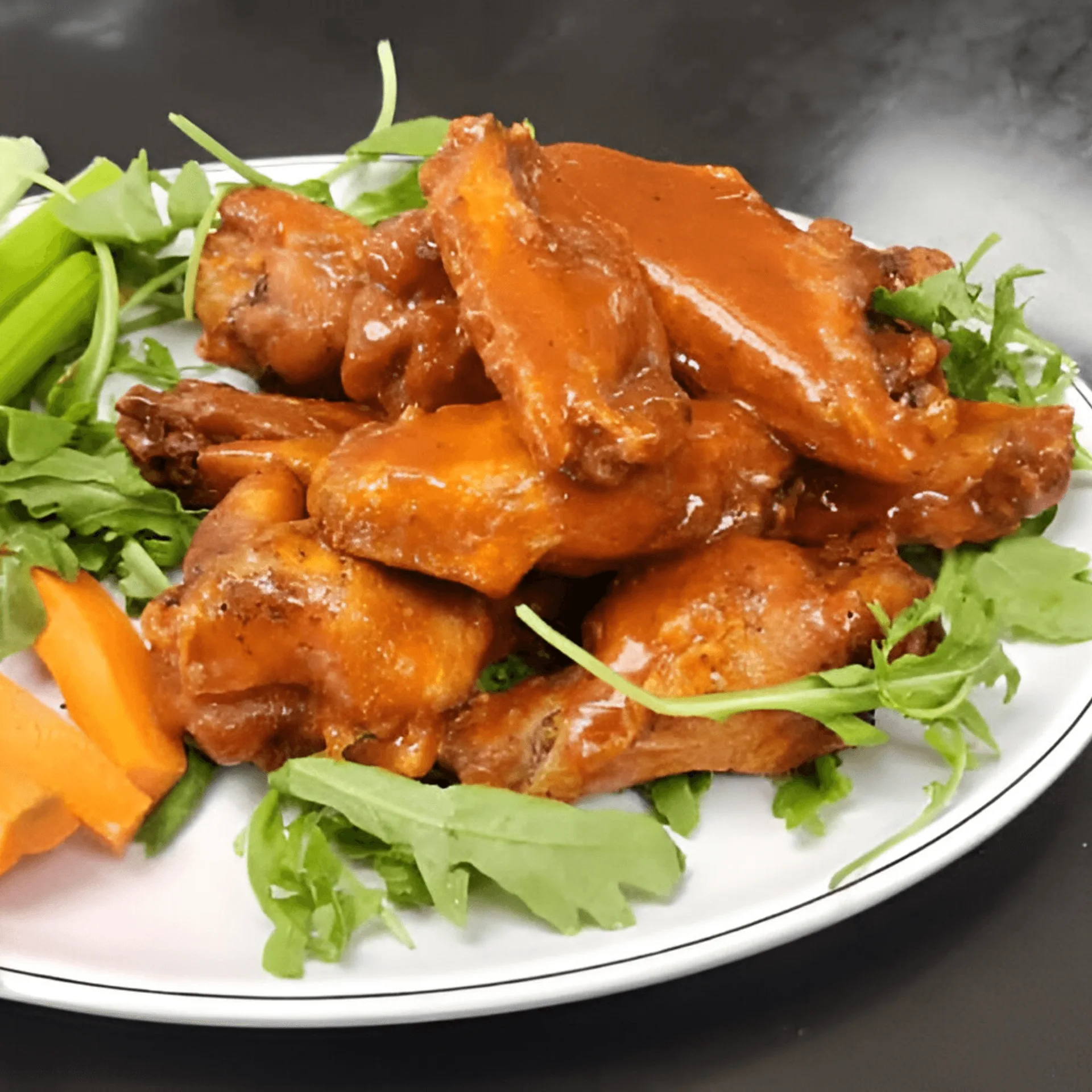 ShortyonDeck's buffalo wings with celery, carrots, and arugula on a white plate.