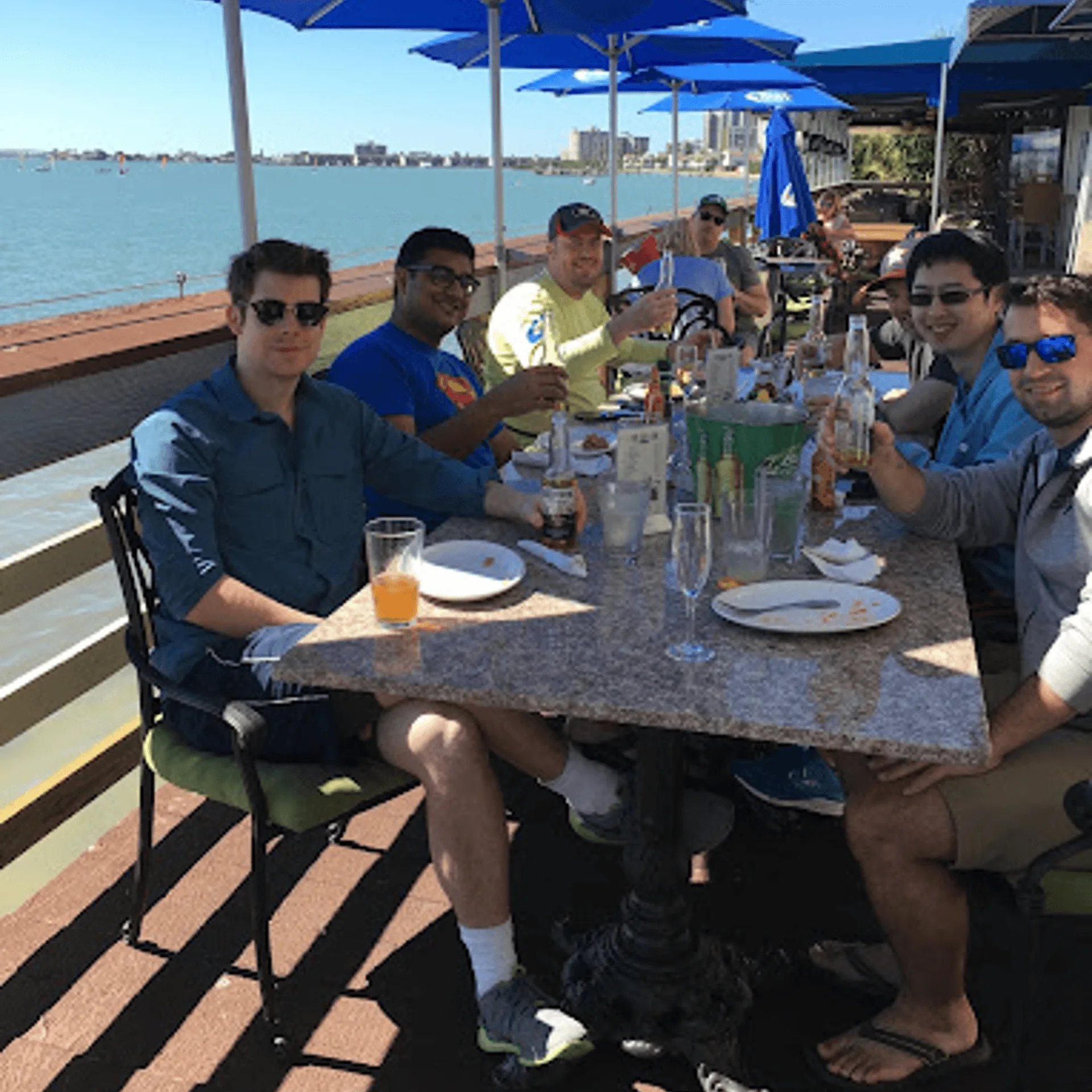 Group of men enjoying drinks and food at an outdoor ShortyonDeck restaurant table overlooking the water.